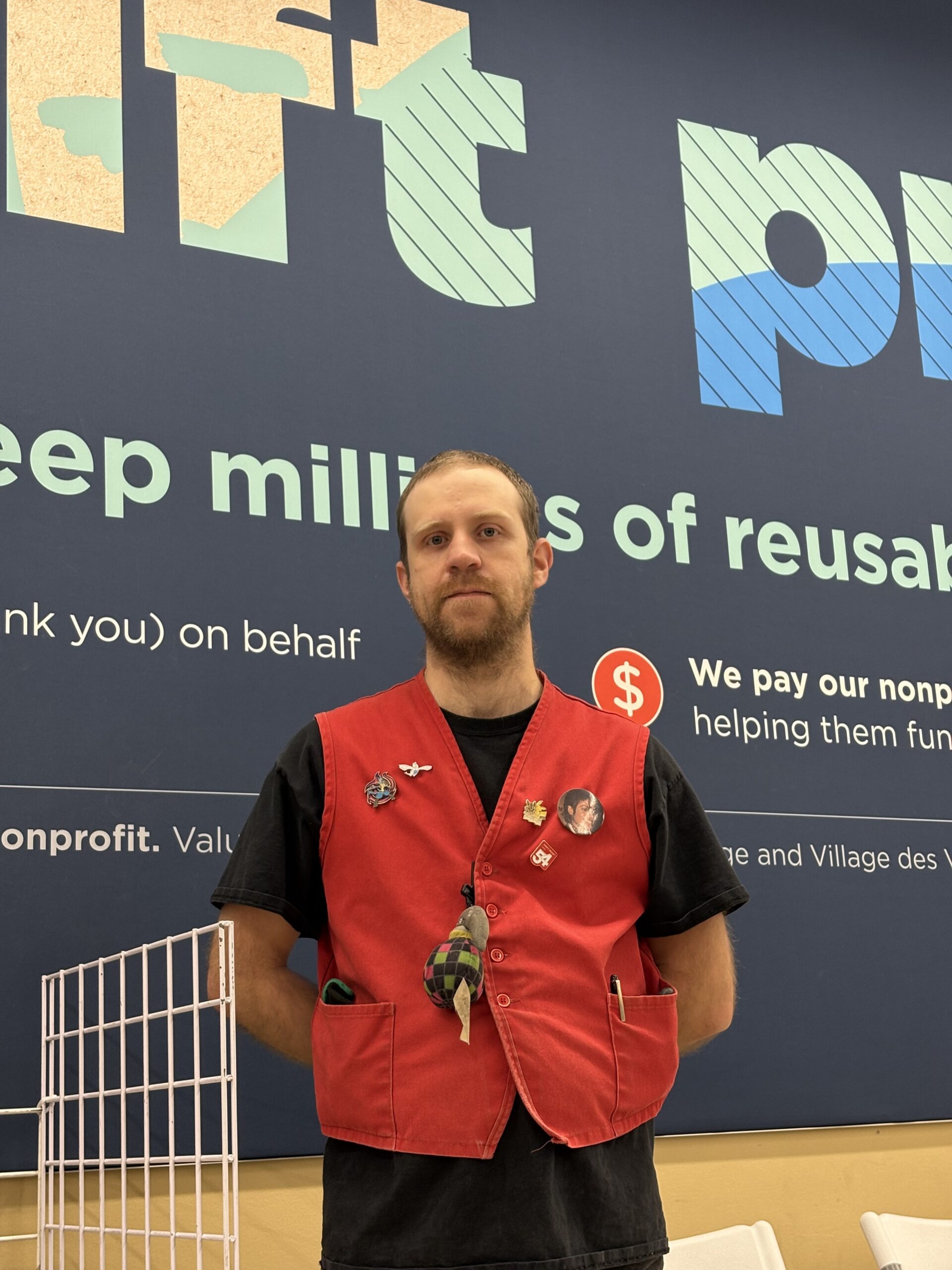 Andrew, wearing a red vest, stands in front of a sign at Value Village